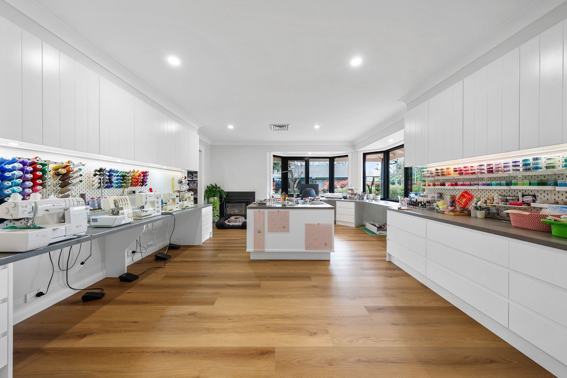 Bright sewing studio with white cabinets, wooden floor, sewing machines, colorful threads, and central work table — Above & Beyond Interiors Custom Joinery in Bellambi, NSW