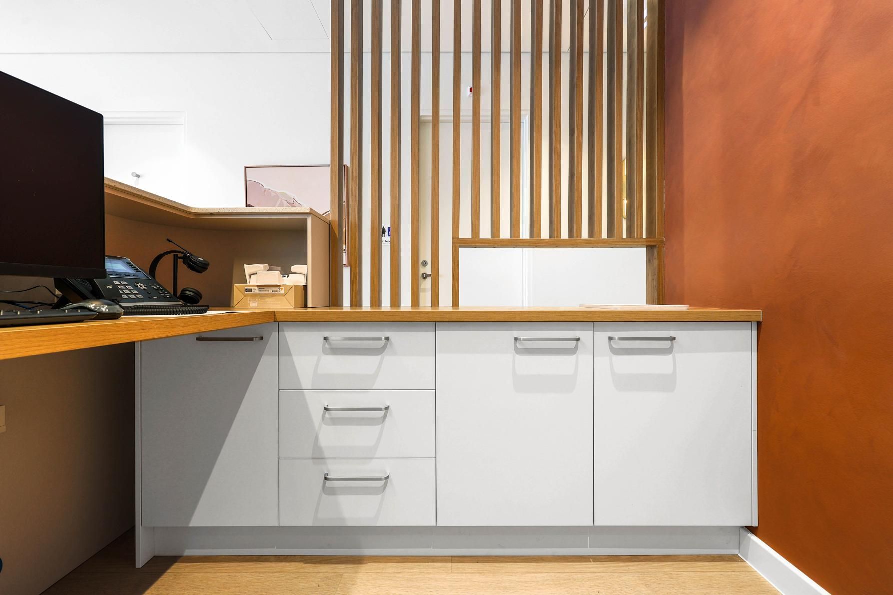 White Cabinets with Silver Handles and Wooden Countertop in A Modern Office with Orange Wall — Above & Beyond Interiors Custom Joinery in Medical Centre, NSW