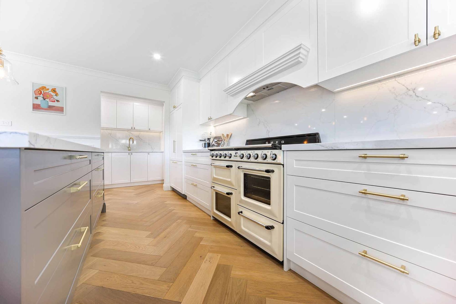 White kitchen with wood herringbone floors, a large oven, and gold hardware — Above & Beyond Interiors Custom Joinery in Bellambi, NSW