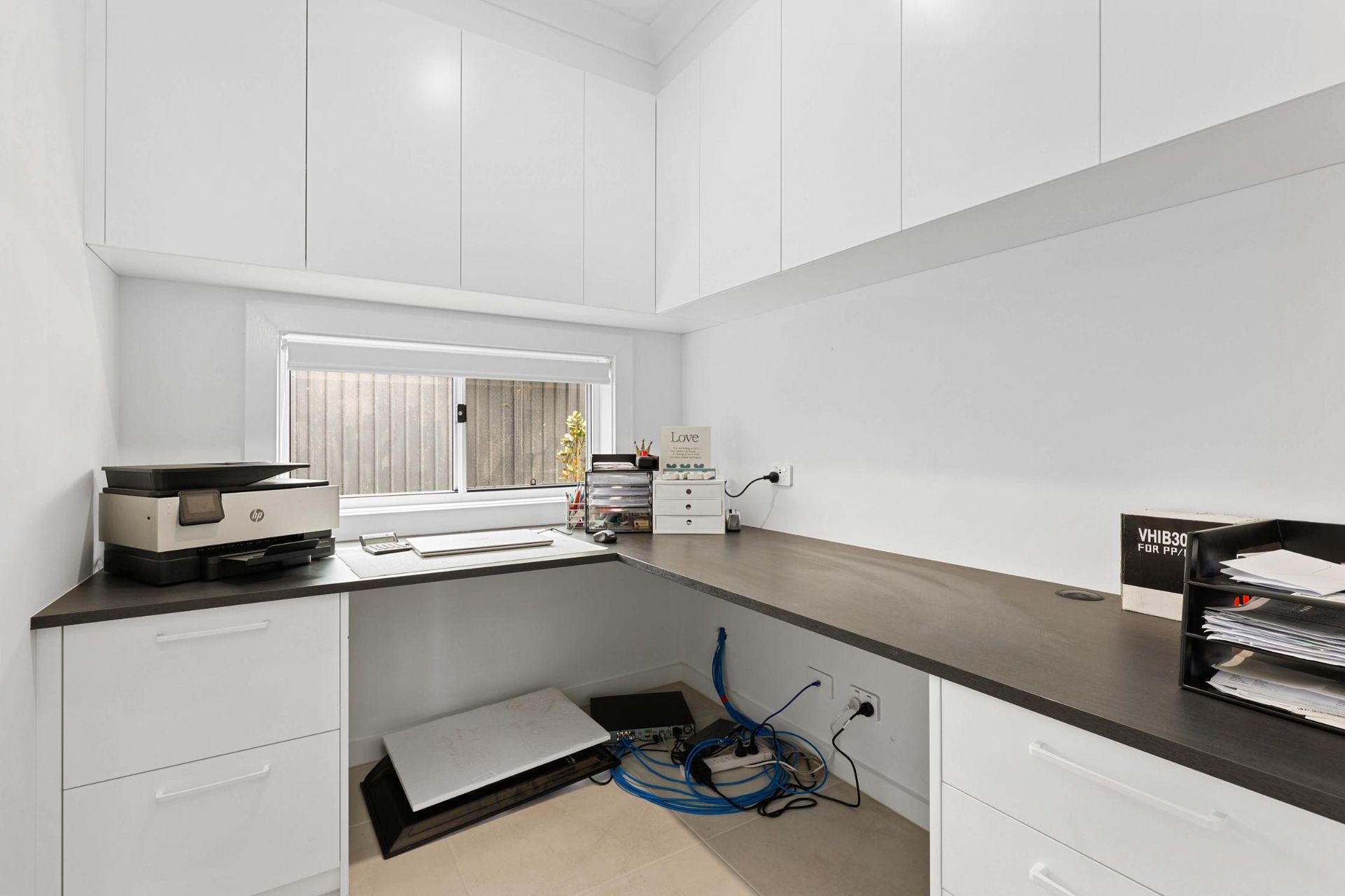 A Small, Modern Home Office with White Cabinets and A Dark Countertop, Window, and Printer — Above & Beyond Interiors Custom Joinery in Currans Hill, NSW
