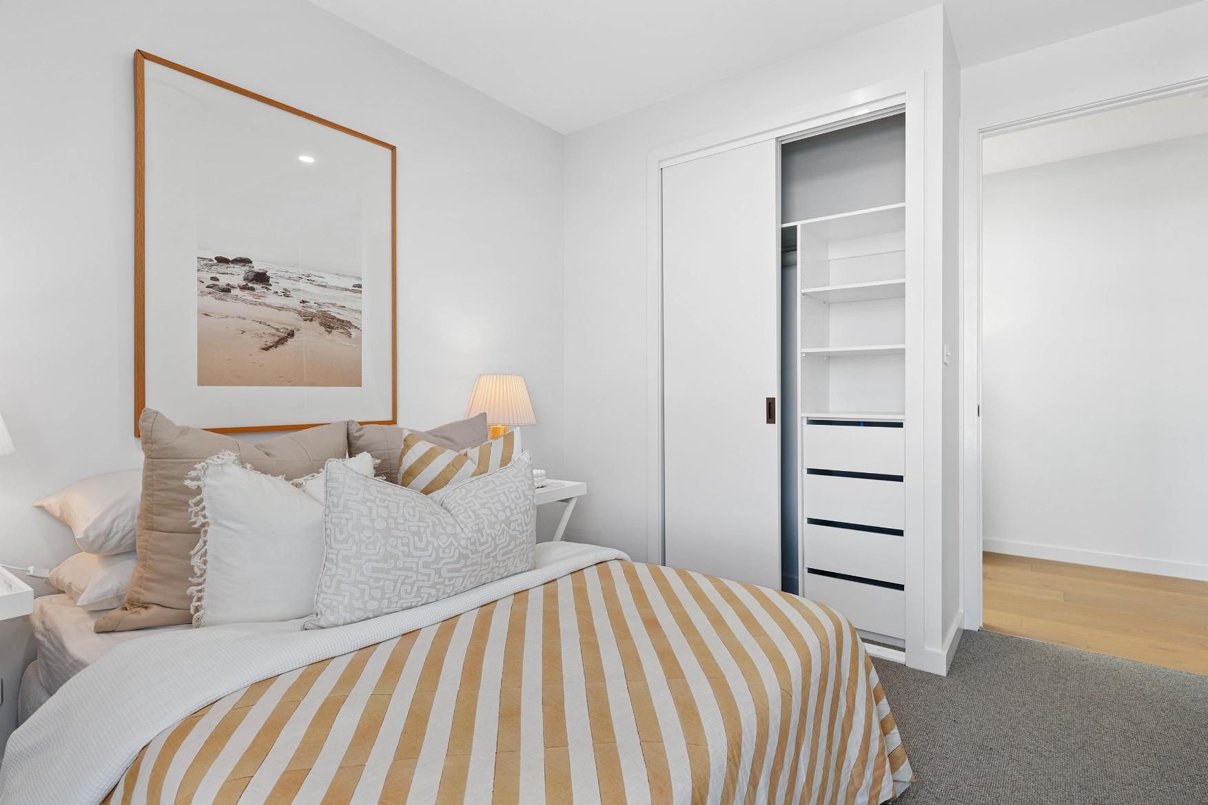 Bedroom with Bed, Side Table, Artwork, Window with Ocean View, and White Closet — Above & Beyond Interiors Custom Joinery in Thirroul, NSW