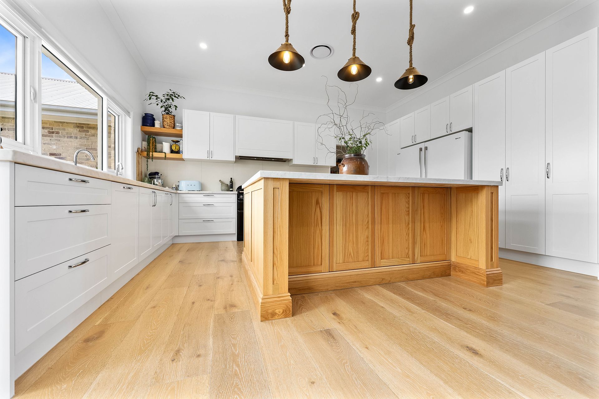 Bright kitchen with wooden island and cabinets, pendant lights, and wood flooring — Above & Beyond Interiors Custom Joinery in Bradbury, NSW