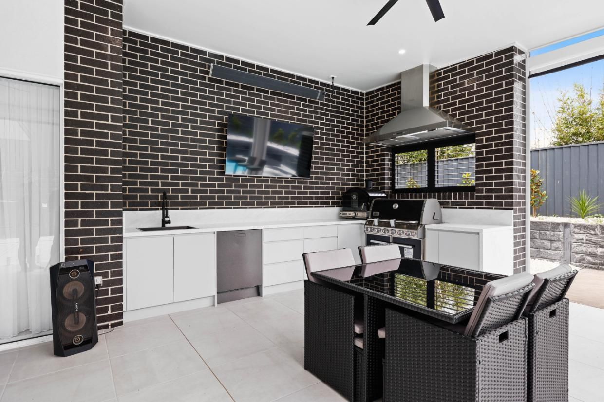 Outdoor Kitchen with Dark Brick Walls, White Cabinets, Black Table, and Grill — Above & Beyond Interiors Custom Joinery in Currans Hill, NSW