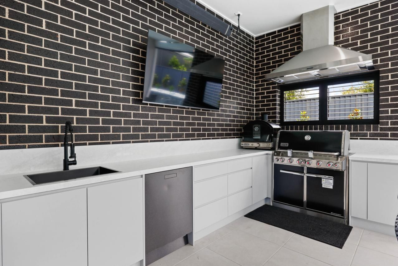 Outdoor Kitchen with Black Brick Walls, White Countertops and Cabinets, and Stainless Steel Appliances — Above & Beyond Interiors Custom Joinery in Currans Hill, NSW