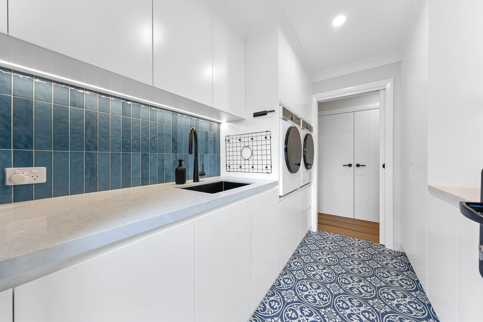 Modern laundry room with white cabinets, blue backsplash, patterned floor, and entry door — Above & Beyond Interiors Custom Joinery in Bellambi, NSW
