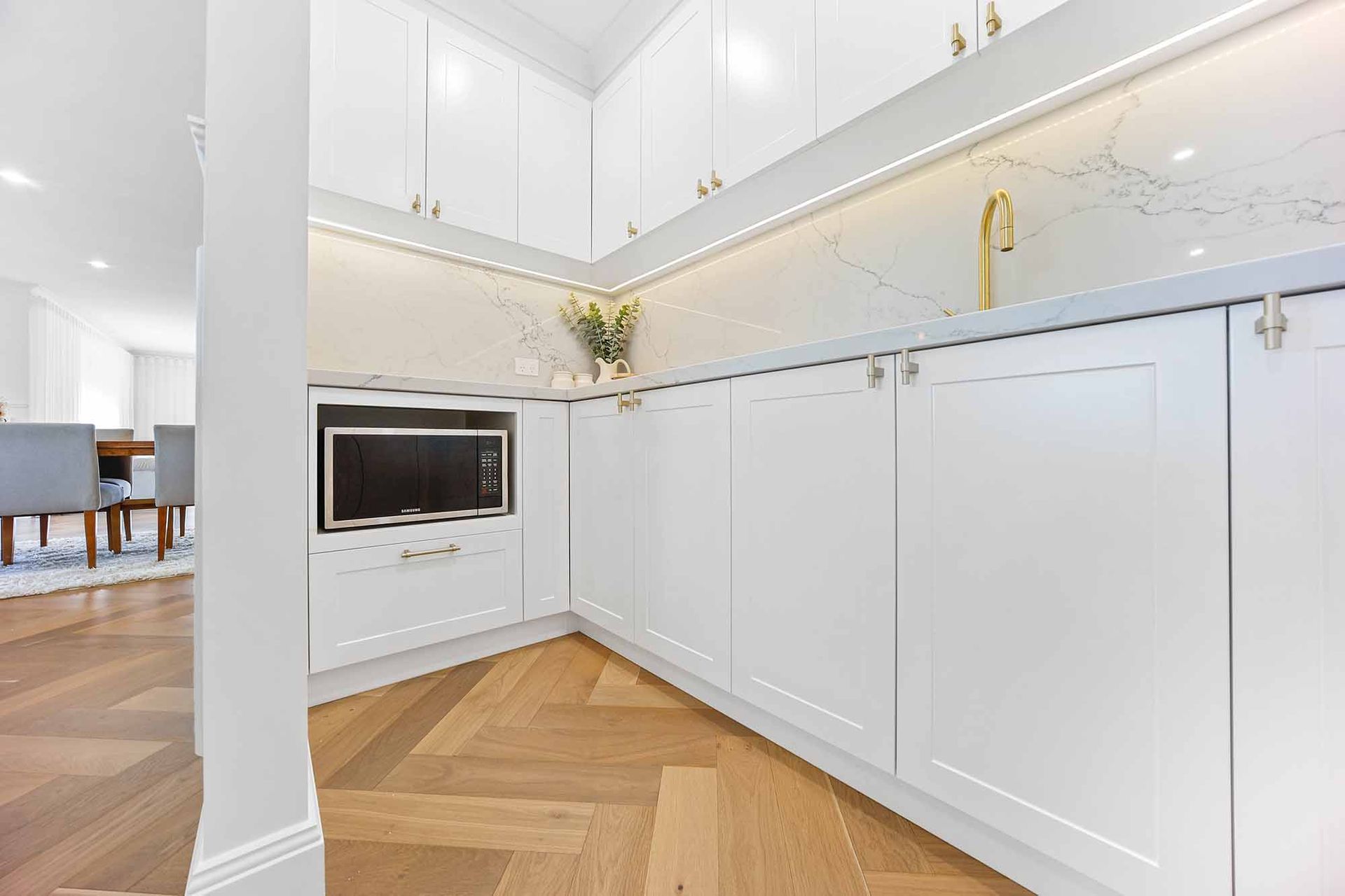 White kitchen with built-in microwave, quartz countertop, and gold faucet, illuminated by LED lights — Above & Beyond Interiors Custom Joinery in Bellambi, NSW
