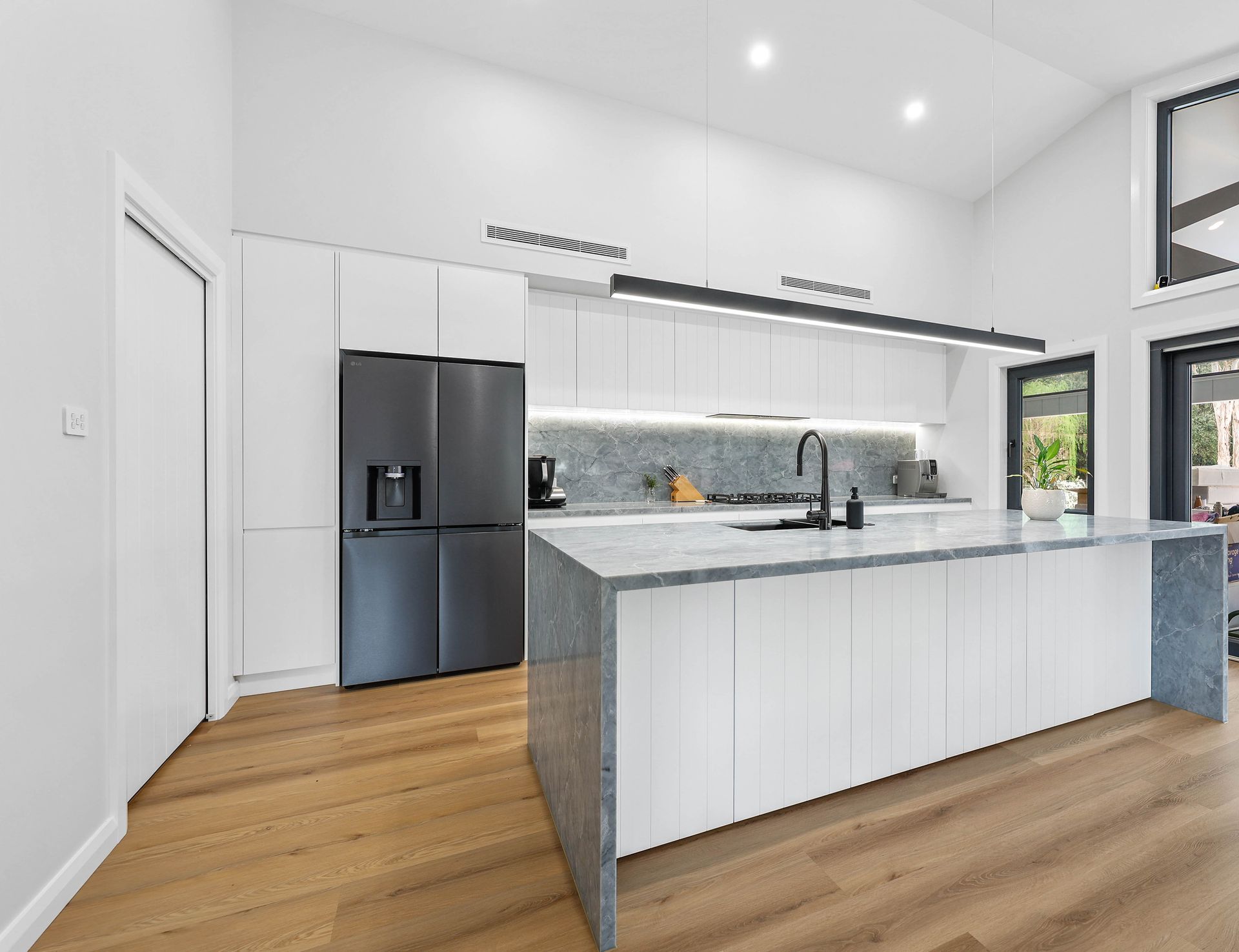 Modern white kitchen with a large island, black appliances, and wood floors — Above & Beyond Interiors in Wollongong, NSW