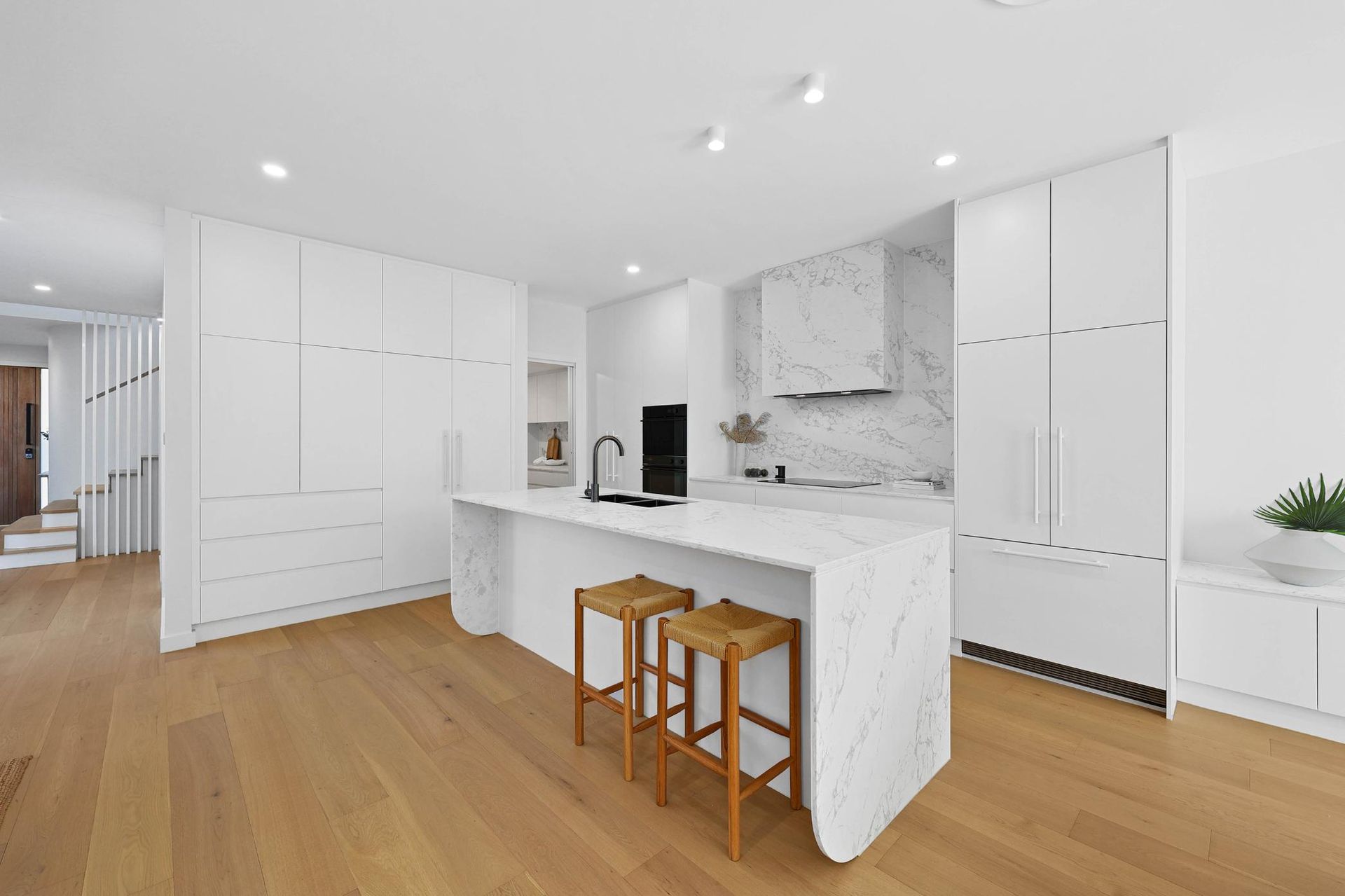 Modern White Kitchen with Marble Island and Wood Flooring. Two Stools Sit at The Island — Above & Beyond Interiors Custom Joinery in Thirroul, NSW