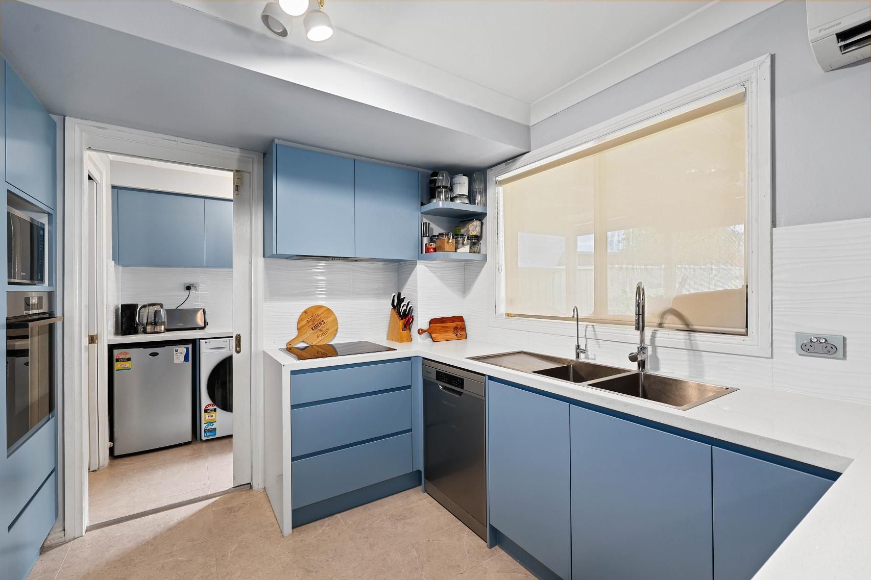 Blue Kitchen with White Countertops, Stainless Steel Appliances, and A Window with A Beige Blind — Above & Beyond Interiors Custom Joinery in Macquarie Fields, NSW