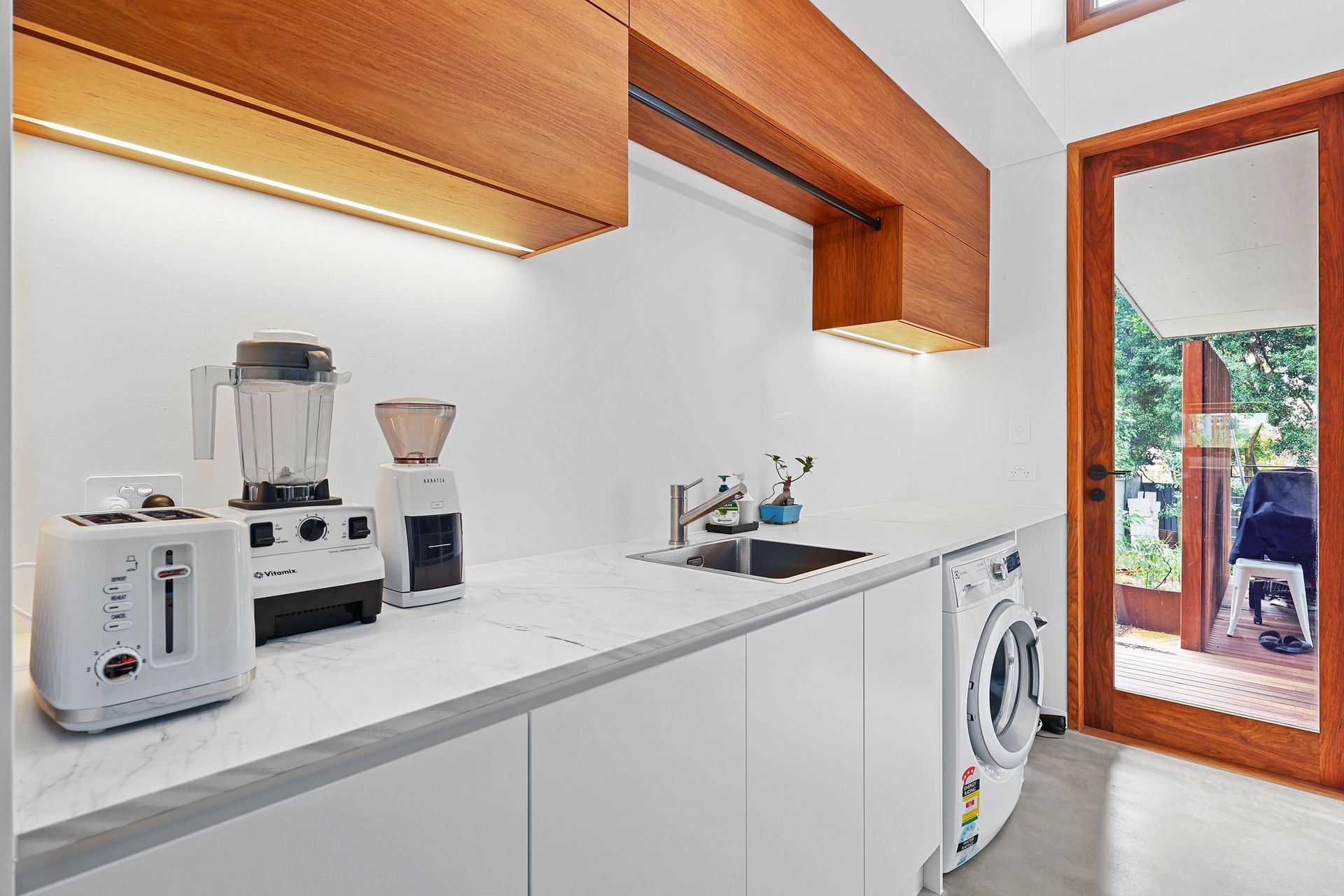 White laundry room with wooden accents, appliances on countertop, and a view of the outdoors — Above & Beyond Interiors Custom Joinery in Bellambi, NSW