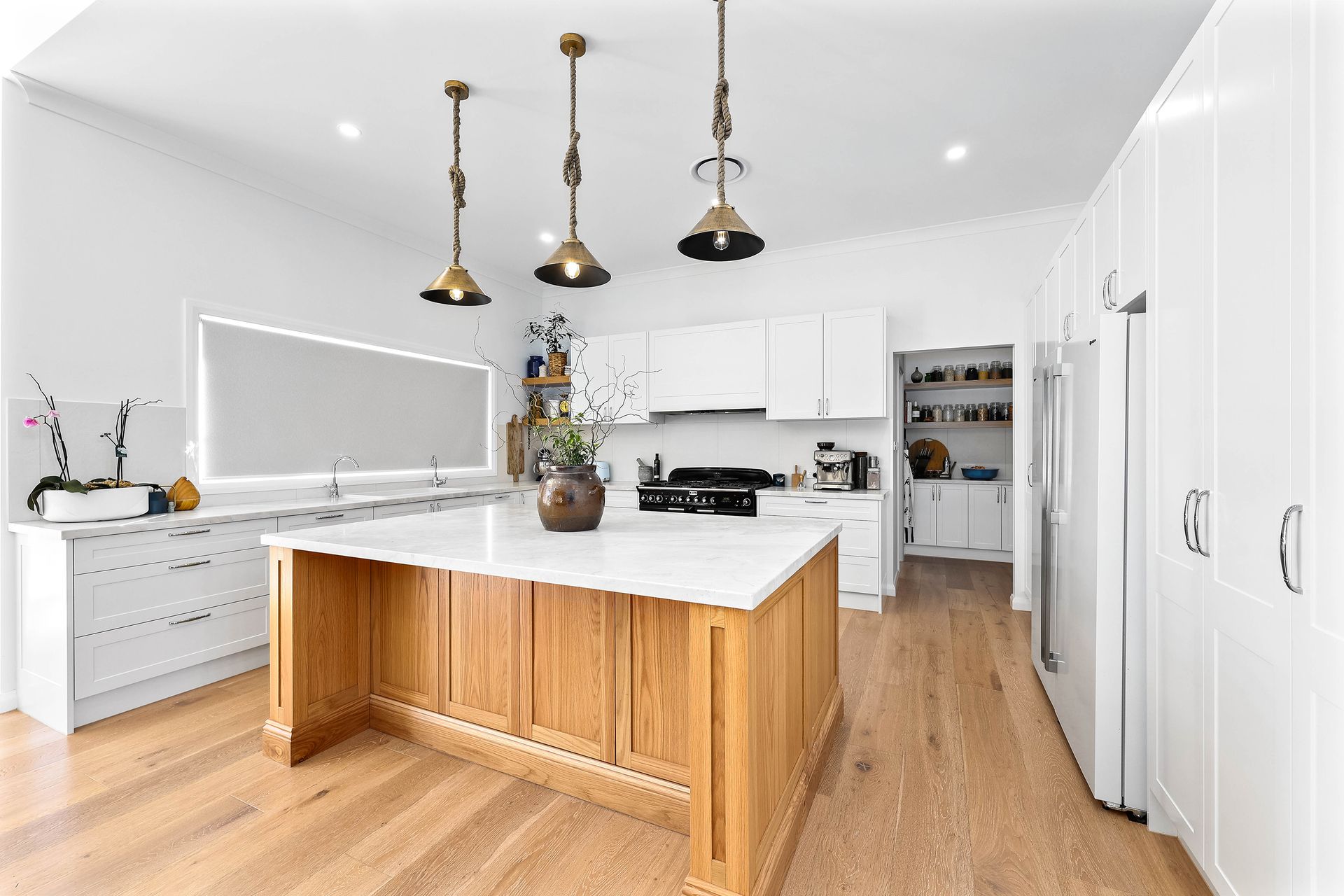 Bright white kitchen with a wooden island and pendant lights — Above & Beyond Interiors Custom Joinery in Bradbury, NSW