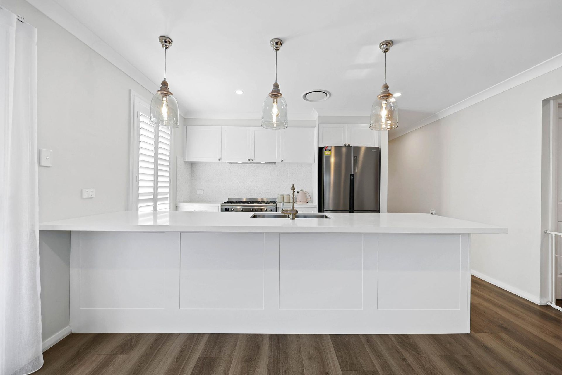 Modern White Kitchen with Island, Pendant Lights, and Stainless Steel Refrigerator — Above & Beyond Interiors Custom Joinery in Thirlmere, NSW