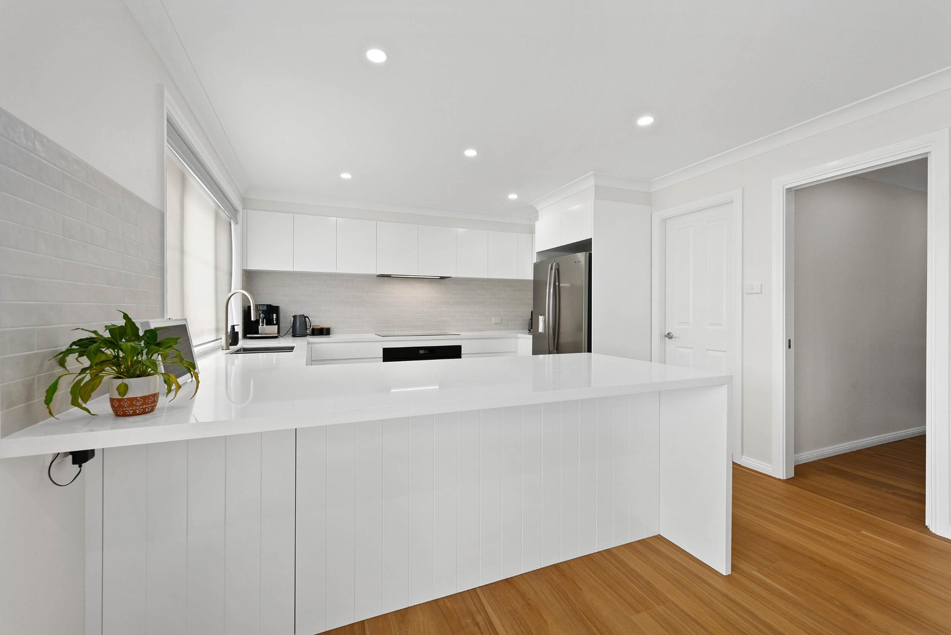 Bright, Modern White Kitchen with Large Island, Stainless Steel Appliances, and Wooden Floors — Above & Beyond Interiors Custom Joinery in Mount Anna, NSW