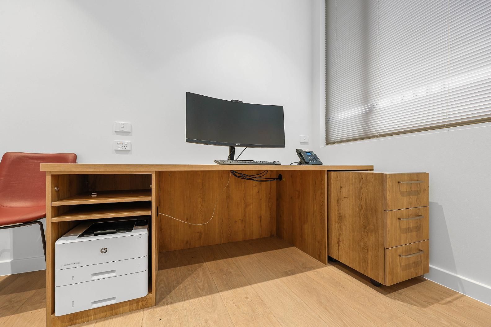 Wooden Office Desk with Computer, Printer, and Drawers. Red Chair to The Left. White Walls, Blinds — Above & Beyond Interiors Custom Joinery in Medical Centre, NSW