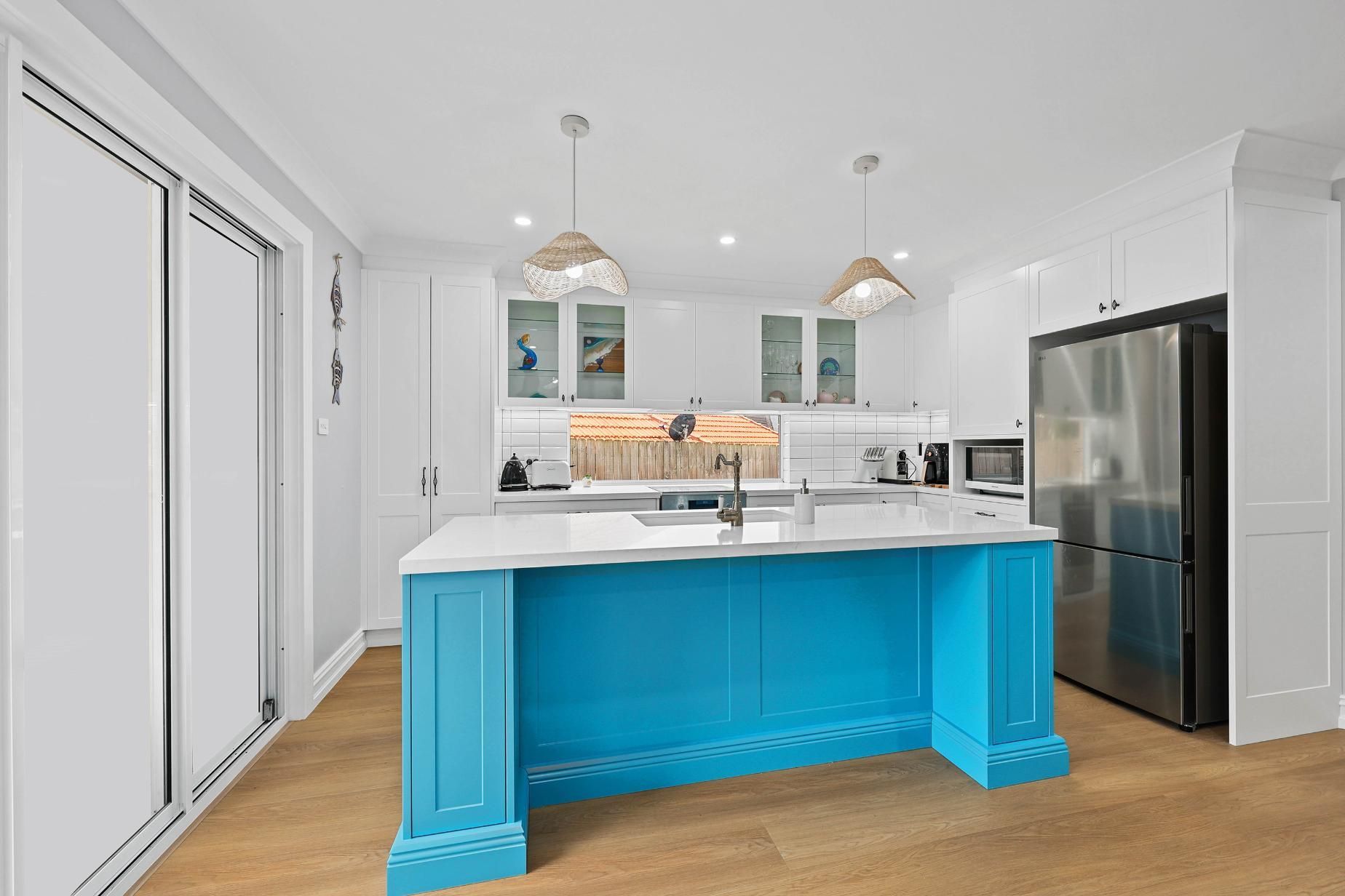 Bright Blue Kitchen Island in A White Kitchen with Wood Flooring and Stainless Steel Appliances — Above & Beyond Interiors Custom Joinery in Gladsville, NSW