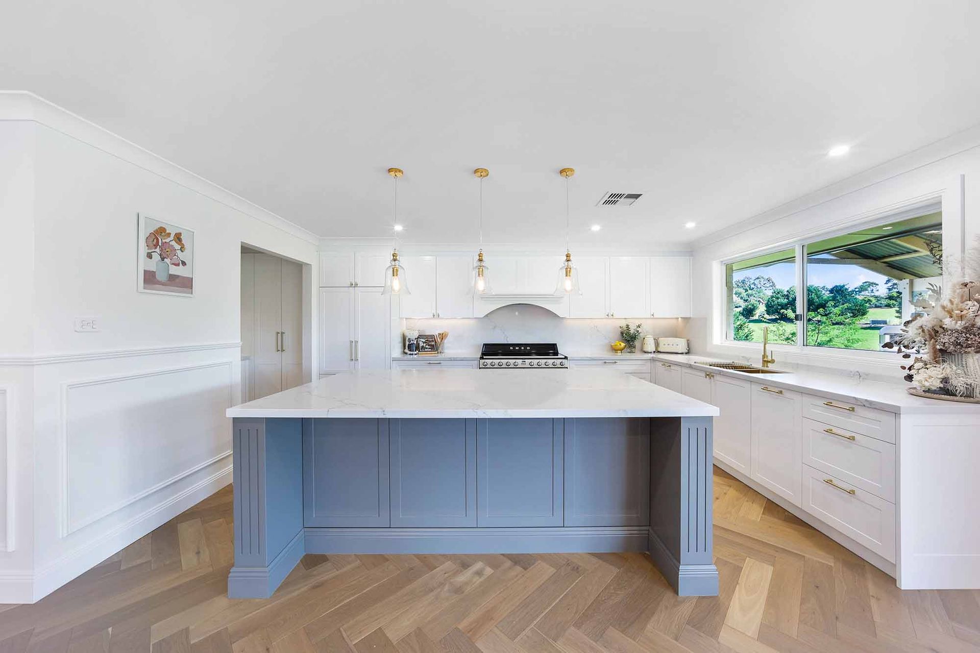 Modern white kitchen with a grey island, gold pendant lights, and a herringbone floor — Above & Beyond Interiors Custom Joinery in Bellambi, NSW