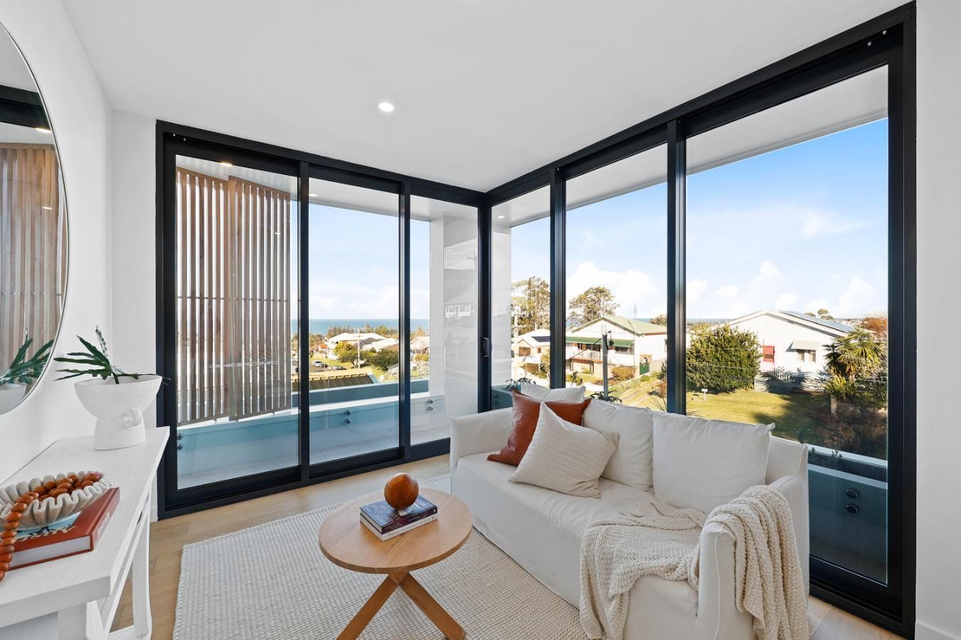 Living Room with White Sofa, Round Table, and Large Windows Overlooking a Coastal View — Above & Beyond Interiors Custom Joinery in Thirroul, NSW