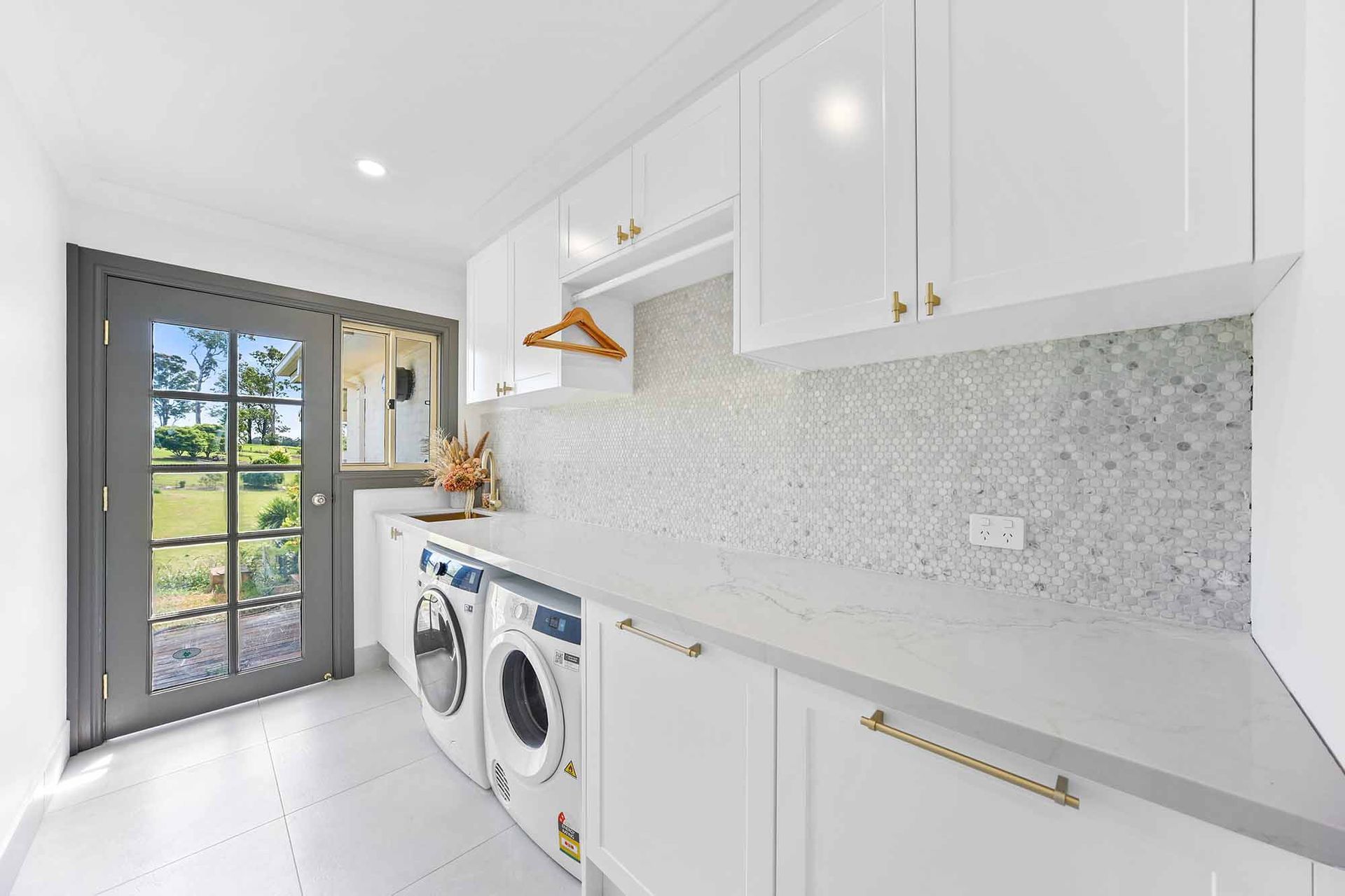 A bright white laundry room with a washing machine, dryer, cabinets, and a door to a backyard — Above & Beyond Interiors Custom Joinery in Bellambi, NSW