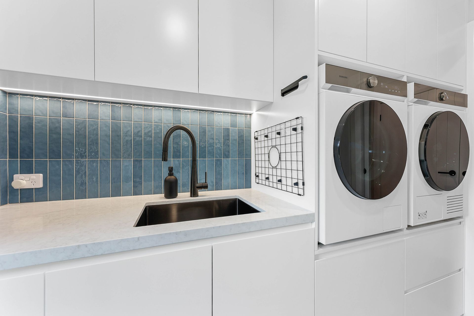 Modern laundry room with blue tile backsplash, black faucet, and white cabinets and appliances — Above & Beyond Interiors Custom Joinery in Bellambi, NSW