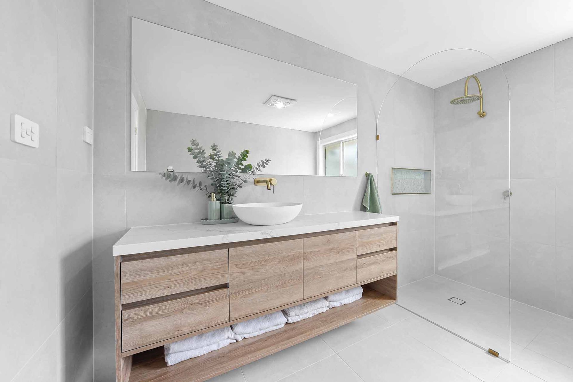 Modern bathroom with light wood vanity, marble countertop, large mirror, glass shower, white and grey tiles — Above & Beyond Interiors Custom Joinery in Bellambi, NSW