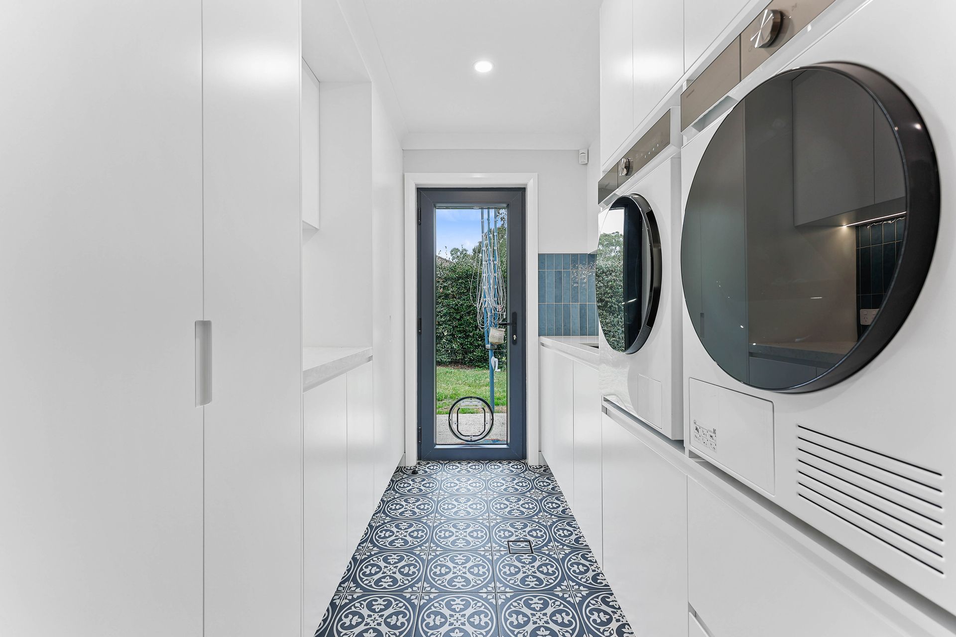 Laundry room with white cabinets, patterned floor, and a door leading outside — Above & Beyond Interiors Custom Joinery in Bellambi, NSW