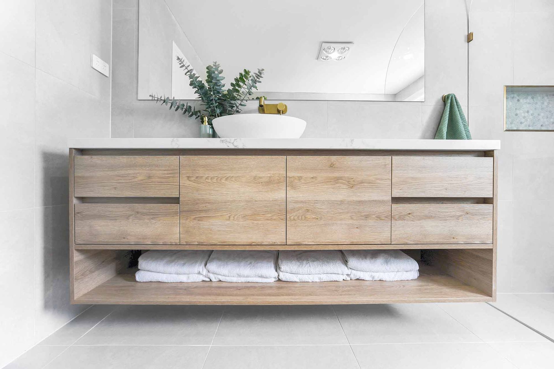 Floating wooden bathroom vanity with sink, mirror, and towels, against a light grey tiled wall — Above & Beyond Interiors Custom Joinery in Bellambi, NSW