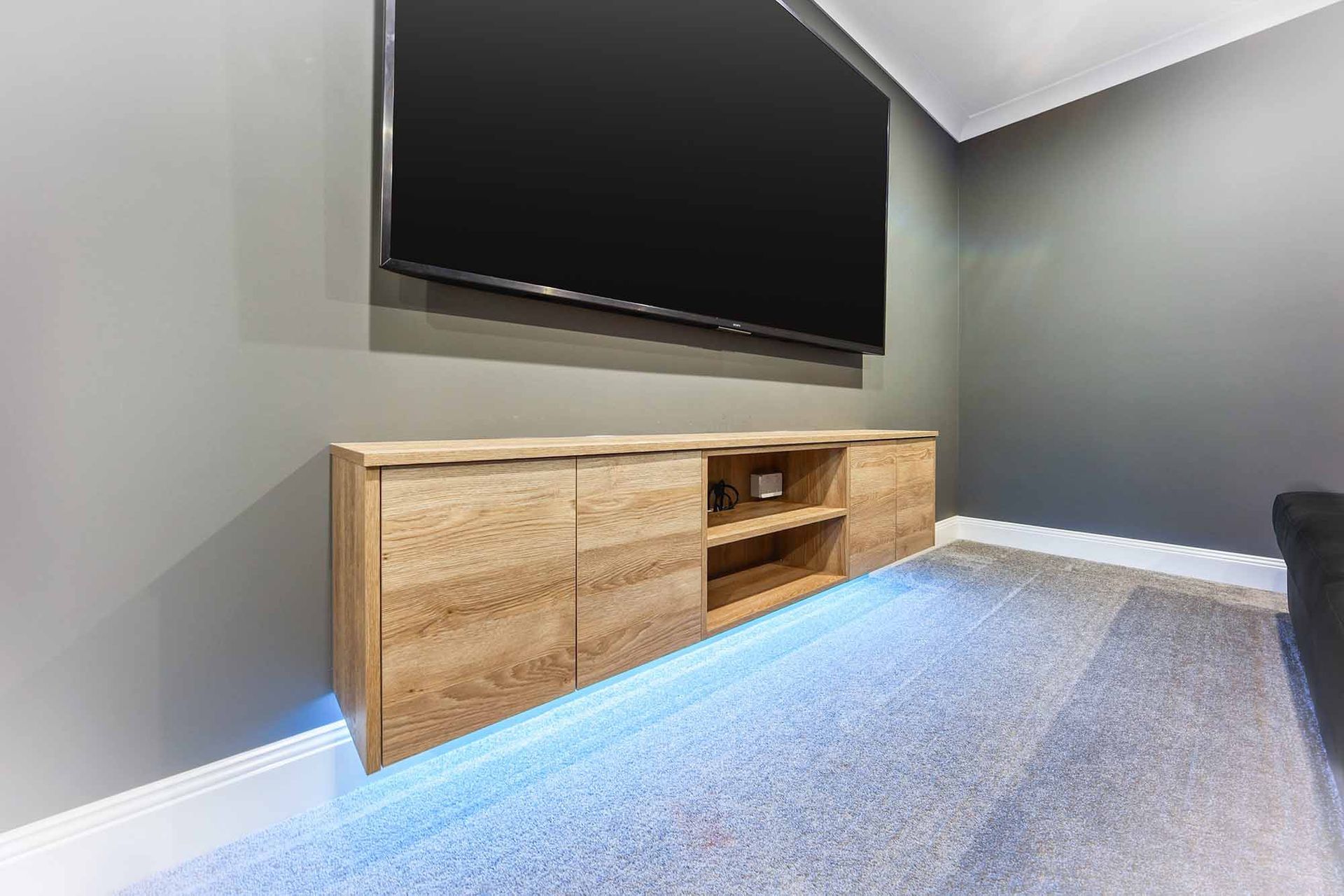 TV mounted above a light wood cabinet on a grey wall. Blue lights illuminate the carpet — Above & Beyond Interiors Custom Joinery in Bellambi, NSW