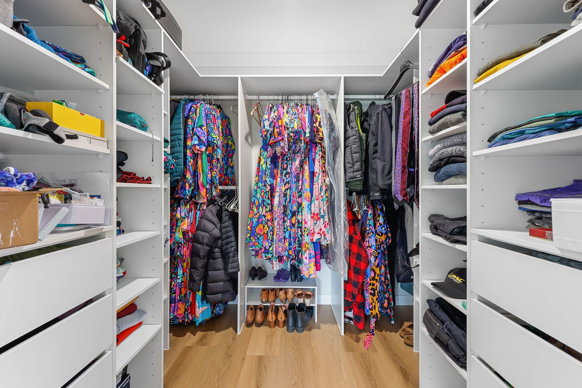 Walk-in closet with white shelves and drawers, clothes hanging, and shoes on the floor — Above & Beyond Interiors Custom Joinery in Bellambi, NSW