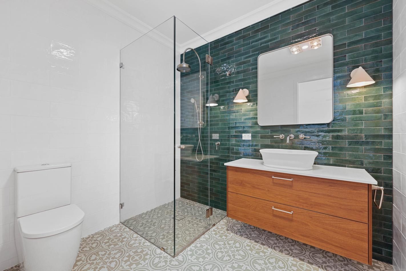 Bathroom with A Green-Tiled Shower, Wooden Vanity, White Toilet, and Patterned Floor — Above & Beyond Interiors Custom Joinery in Appin, NSW