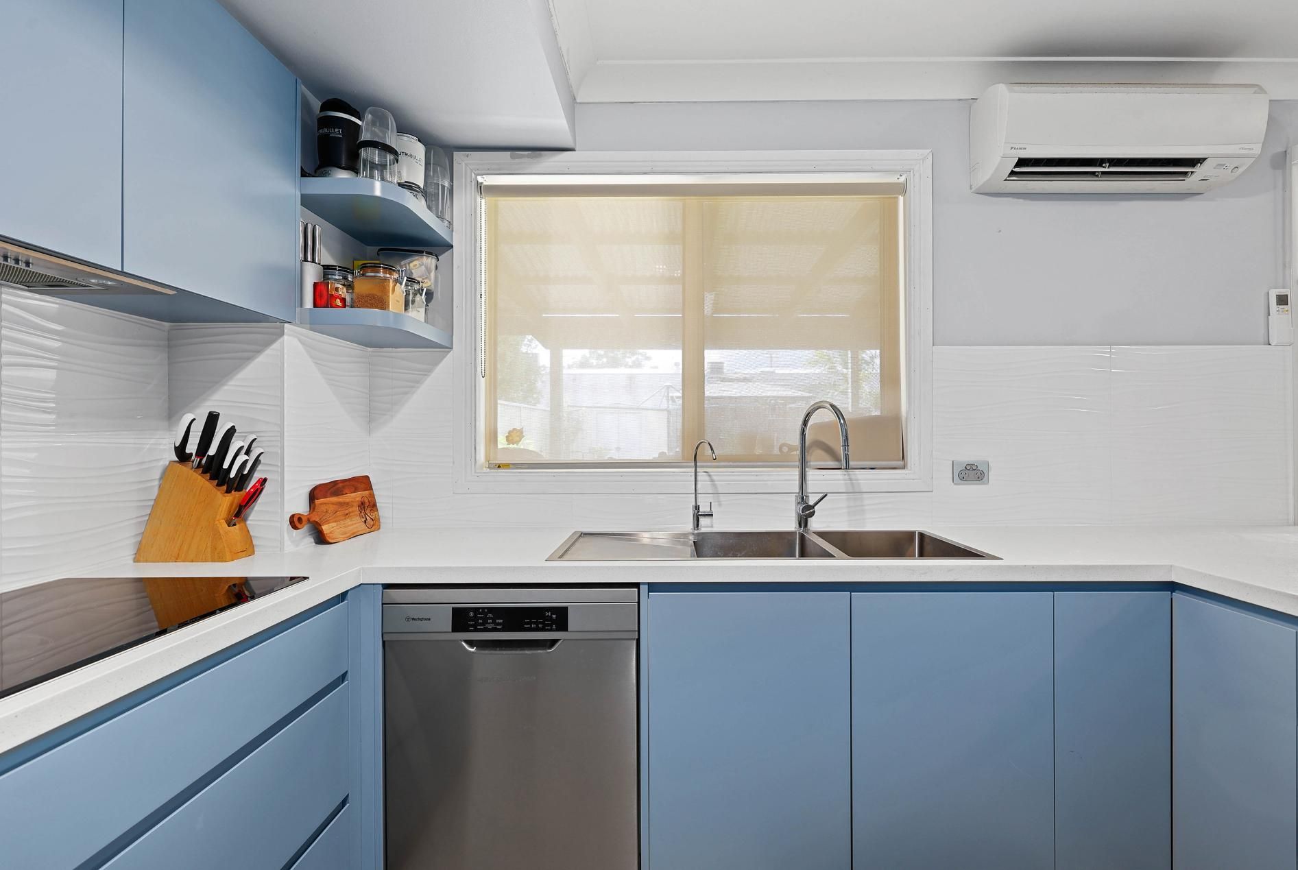 Blue Kitchen Cabinets with White Countertops and Backsplash, a Window, and A Stainless Steel Dishwasher — Above & Beyond Interiors Custom Joinery in Macquarie Fields, NSW