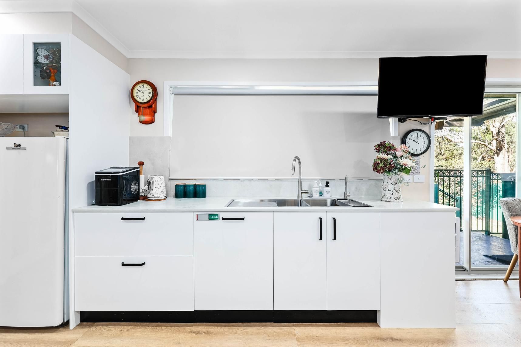 White Kitchen with Appliances, a Clock, and A View of A Balcony — Above & Beyond Interiors Custom Joinery in Bradbury, NSW