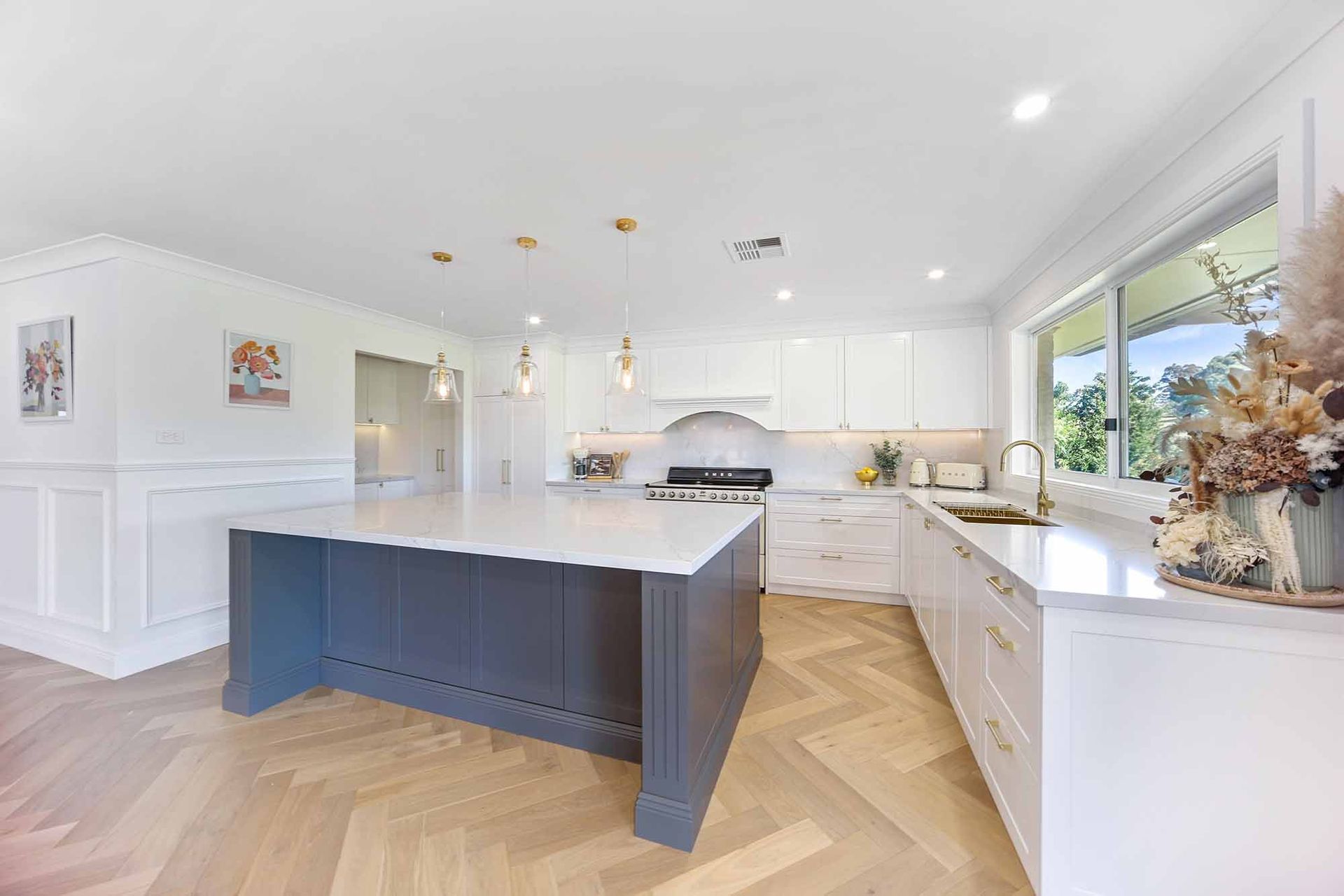 Modern kitchen with a large grey island, white cabinets, and herringbone wood floors — Above & Beyond Interiors Custom Joinery in Bellambi, NSW