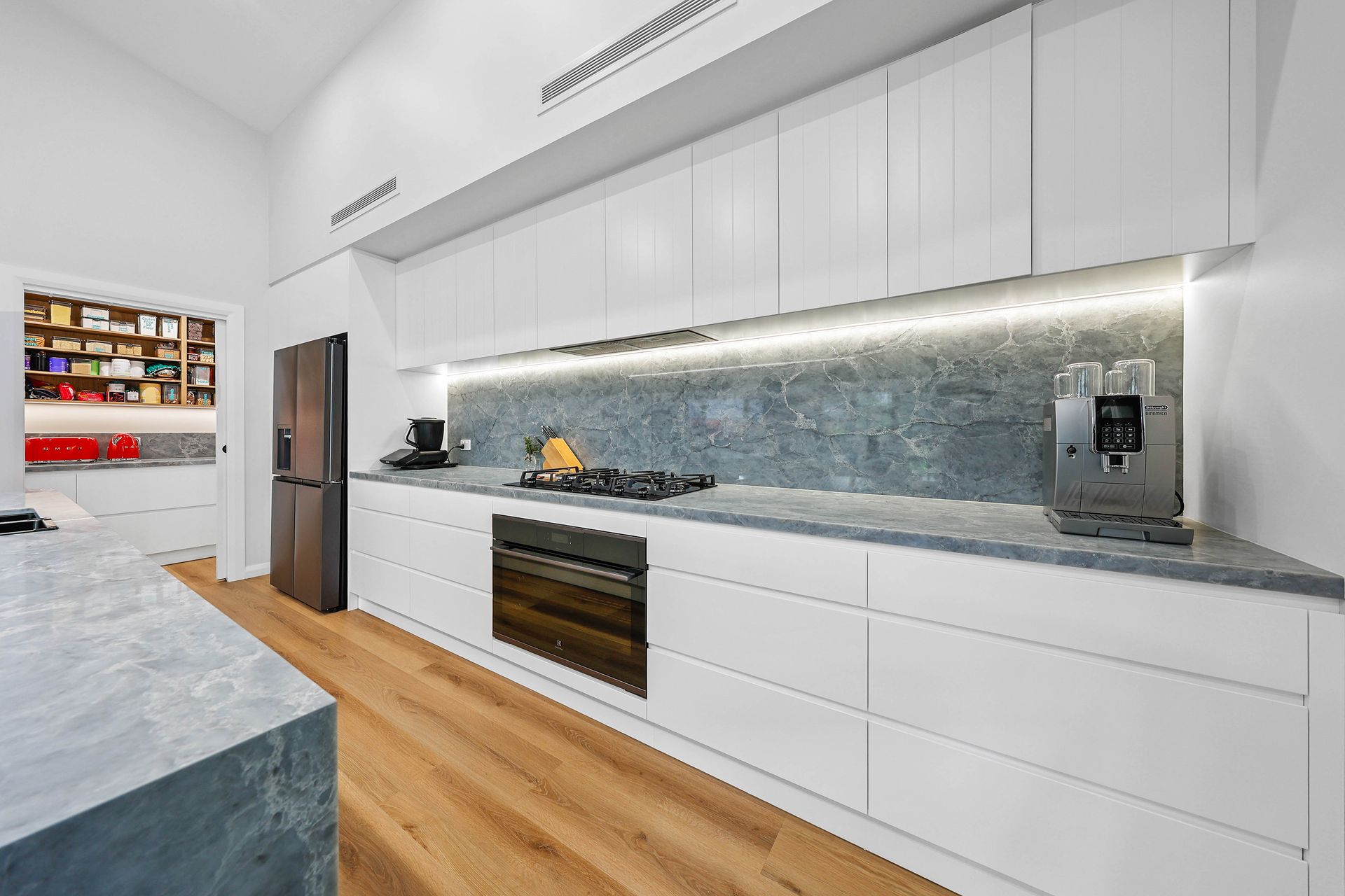Modern white kitchen with grey countertops, stainless steel appliances, and a pantry visible — Above & Beyond Interiors Custom Joinery in Bellambi, NSW