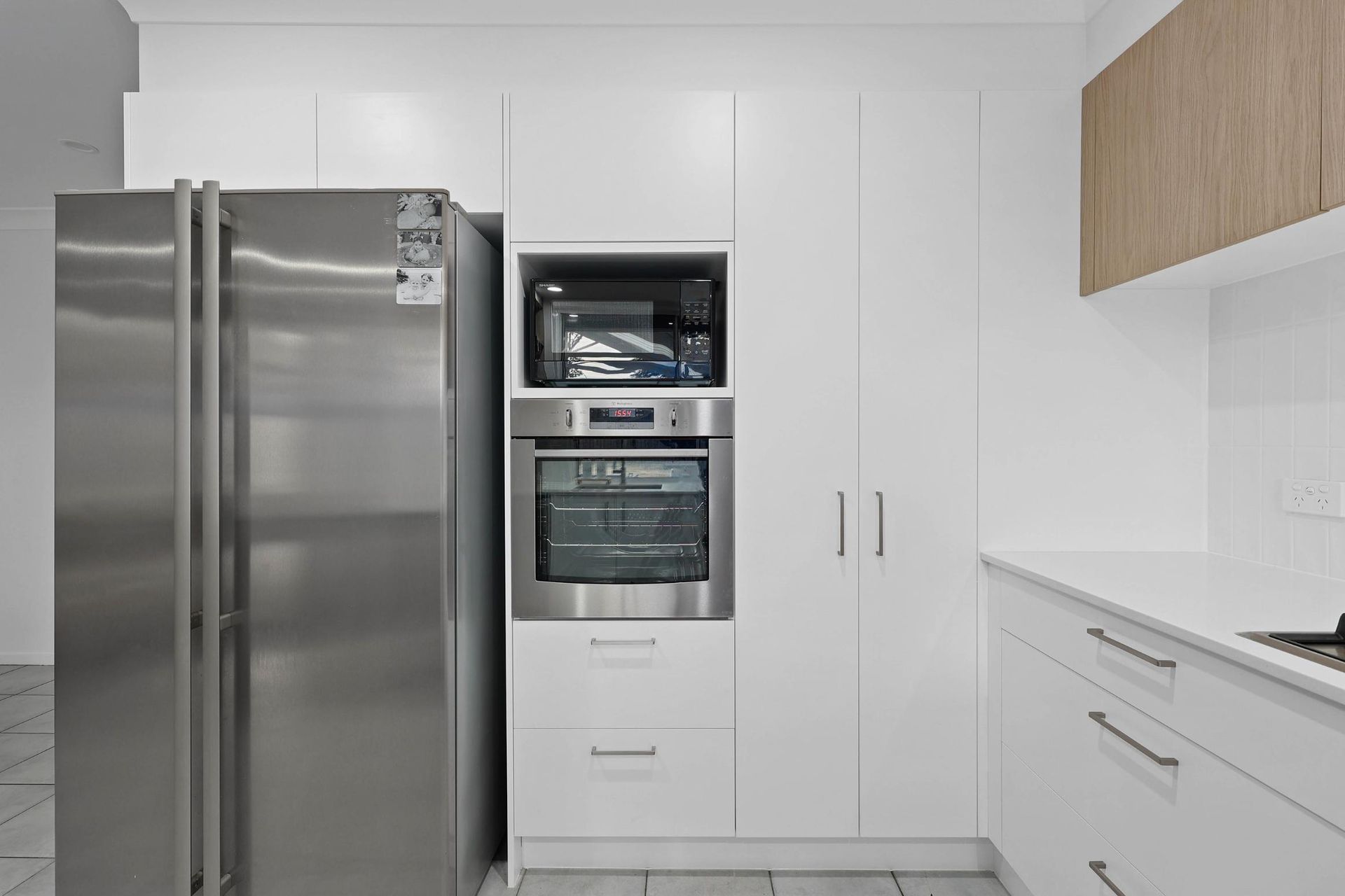 Stainless Steel Refrigerator Next to White Cabinetry with Built-In Microwave and Oven, and A White Countertop — Above & Beyond Interiors Custom Joinery in Currans Hill, NSW