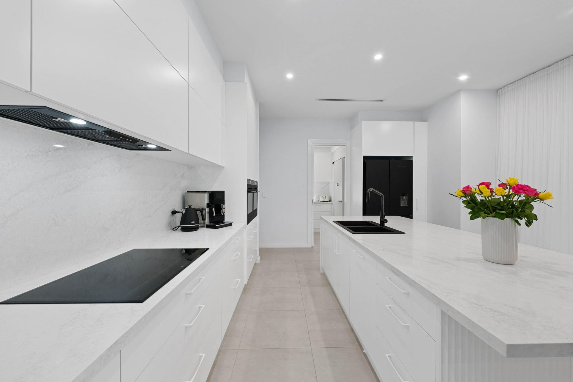 Modern, All-White Kitchen with Island and Countertop, Black Stovetop, and Flower Arrangement — Above & Beyond Interiors Custom Joinery in Currans Hill, NSW