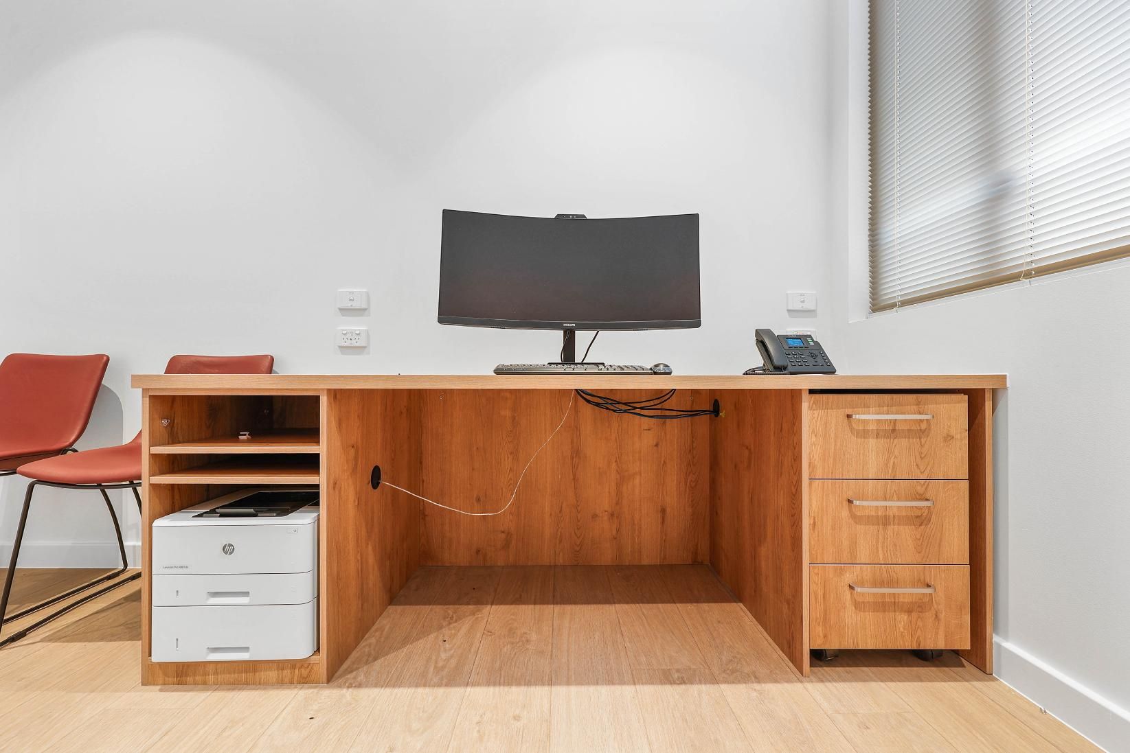 Wooden Desk with Monitor, Printer, Drawers, Telephone; Red Chairs in Office — Above & Beyond Interiors Custom Joinery in Medical Centre, NSW