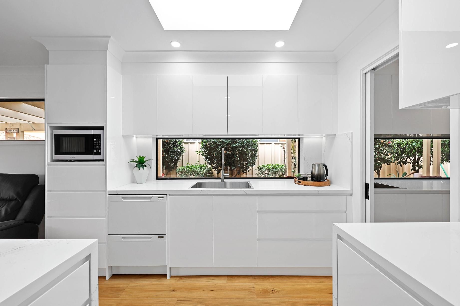 Modern White Kitchen with Sleek Cabinets, Window, and Microwave — Above & Beyond Interiors Custom Joinery in Wattle Grove, NSW