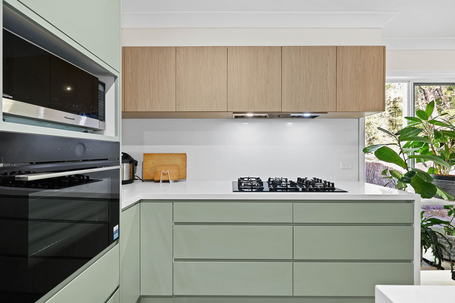 Modern kitchen with light green cabinets, wooden upper cabinets, and built-in appliances — Above & Beyond Interiors Custom Joinery in Bellambi, NSW