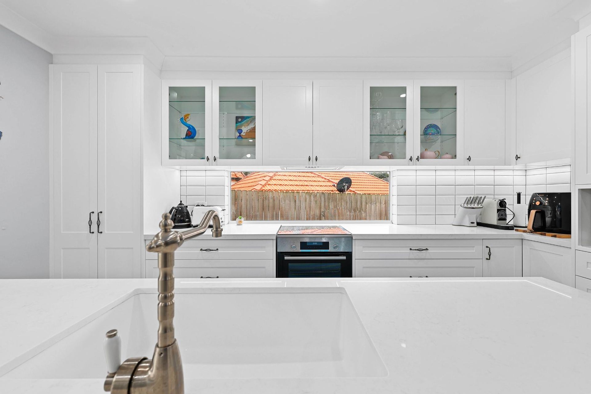 White Kitchen with Cabinets, Countertop, and Stainless Steel Faucet. Oven, Window, and Back Splash Are Visible — Above & Beyond Interiors Custom Joinery in Gladsville, NSW