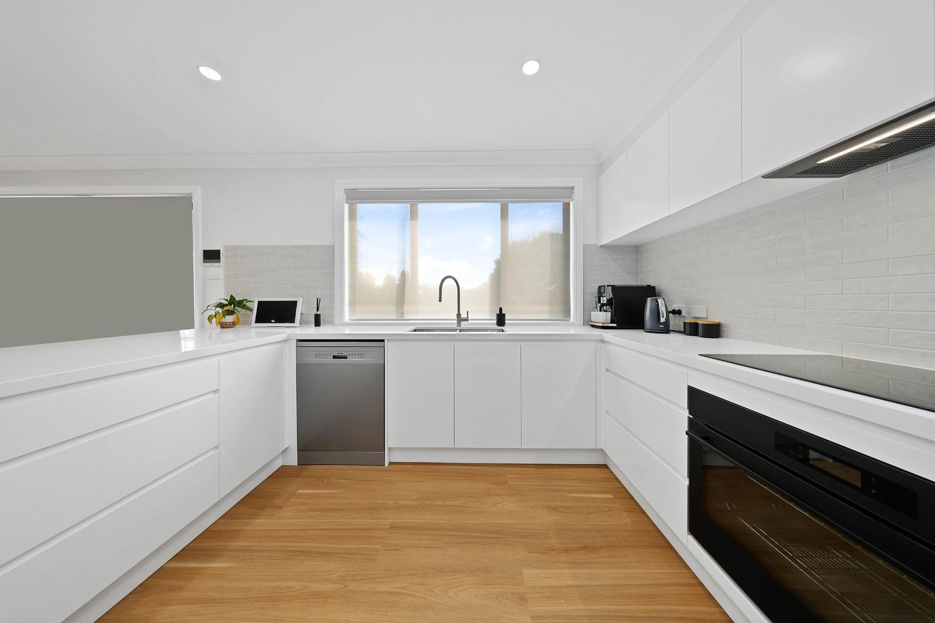 White Modern Kitchen with Wooden Floors, Stainless Steel Appliances, and A Window — Above & Beyond Interiors Custom Joinery in Mount Anna, NSW