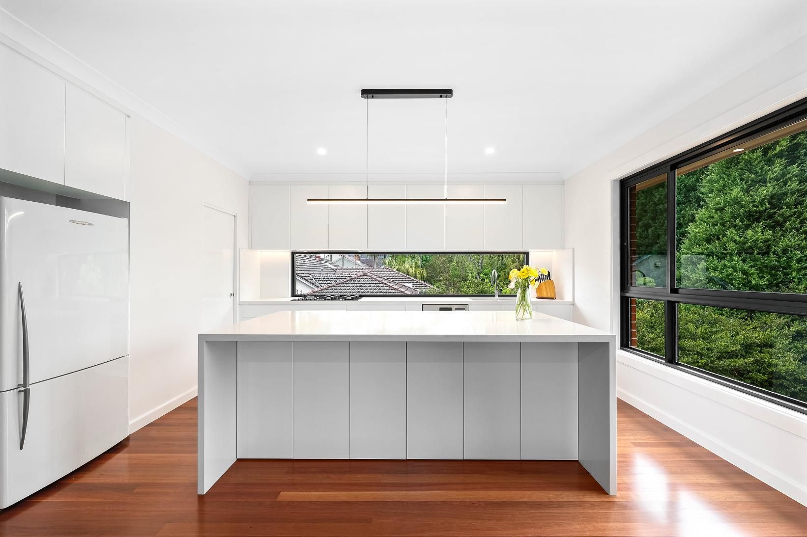 Modern White Kitchen with A Large Island and A View of Trees Through a Window — Above & Beyond Interiors Custom Joinery in Killara, NSW