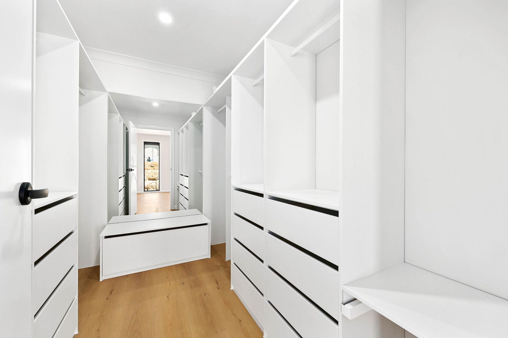 White Walk-In Closet with Wooden Floor, Drawers, Shelves, and Bench in The Center — Above & Beyond Interiors Custom Joinery in Abbortsbury, NSW
