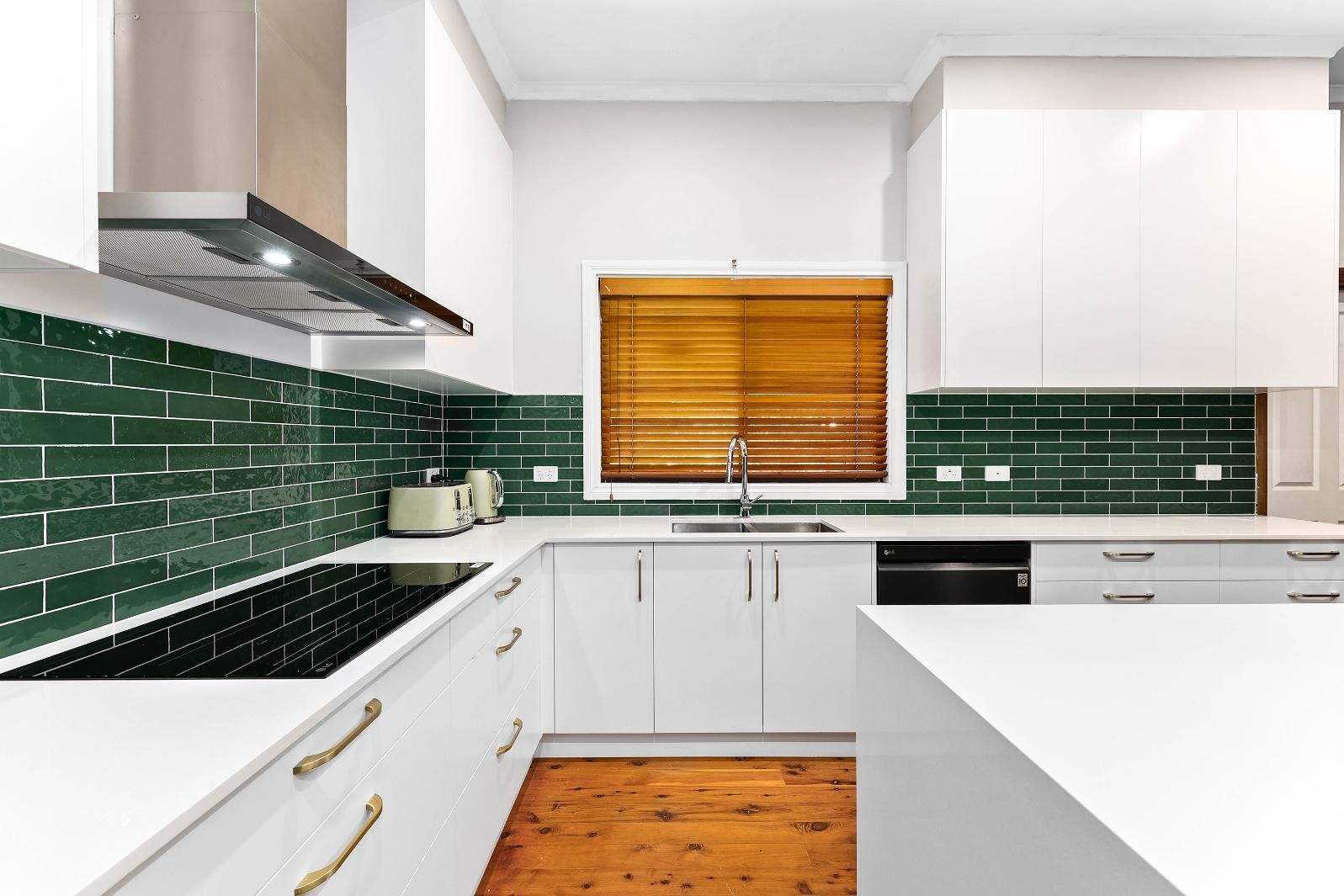 Modern Kitchen with White Cabinets, Green Tile Backsplash, Stainless Steel Range Hood, and Wooden Blinds — Above & Beyond Interiors Custom Joinery in Minto, NSW