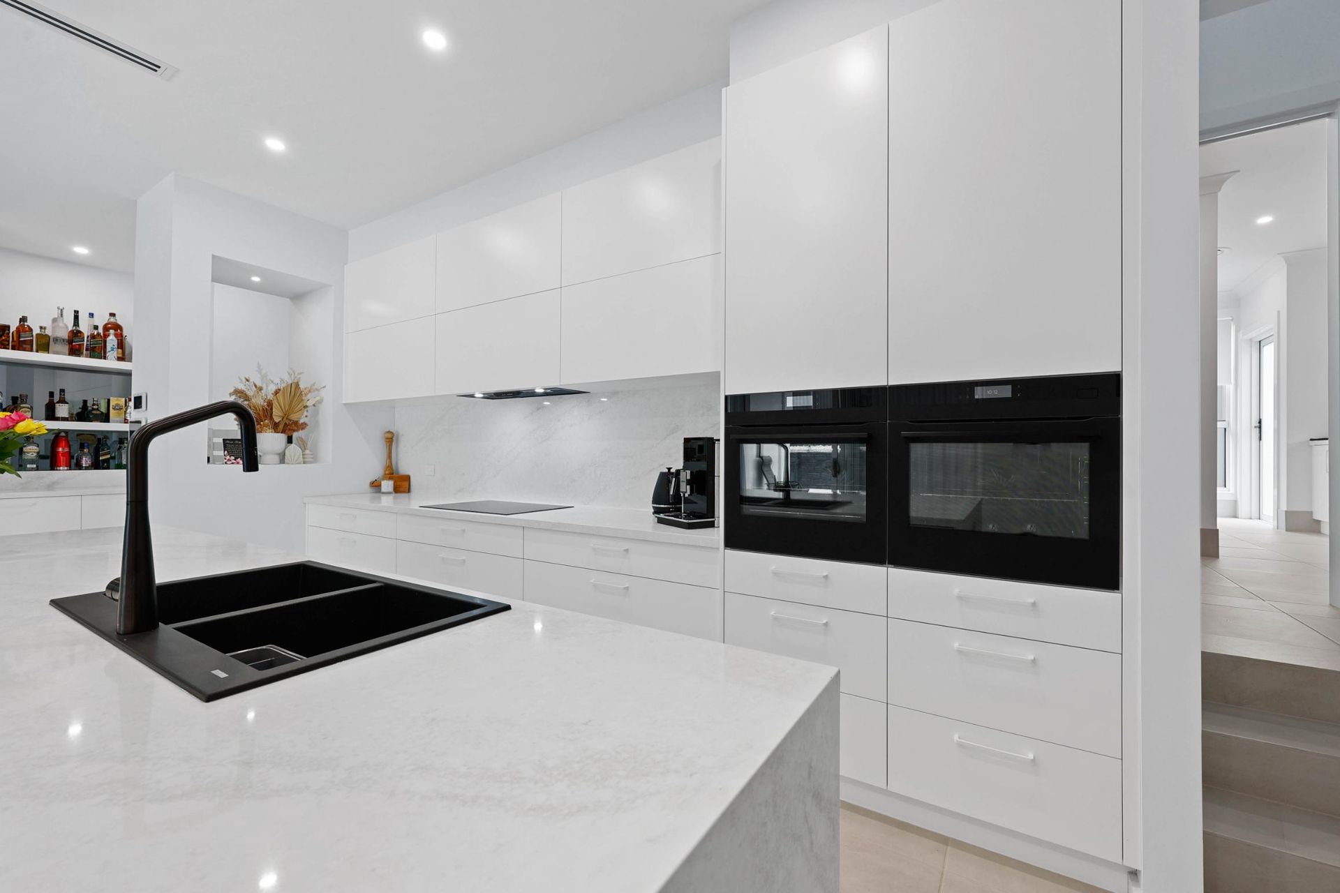 Modern White Kitchen with Black Accents; Island with Sink, Built-In Ovens, and A Hallway Entrance — Above & Beyond Interiors Custom Joinery in Currans Hill, NSW