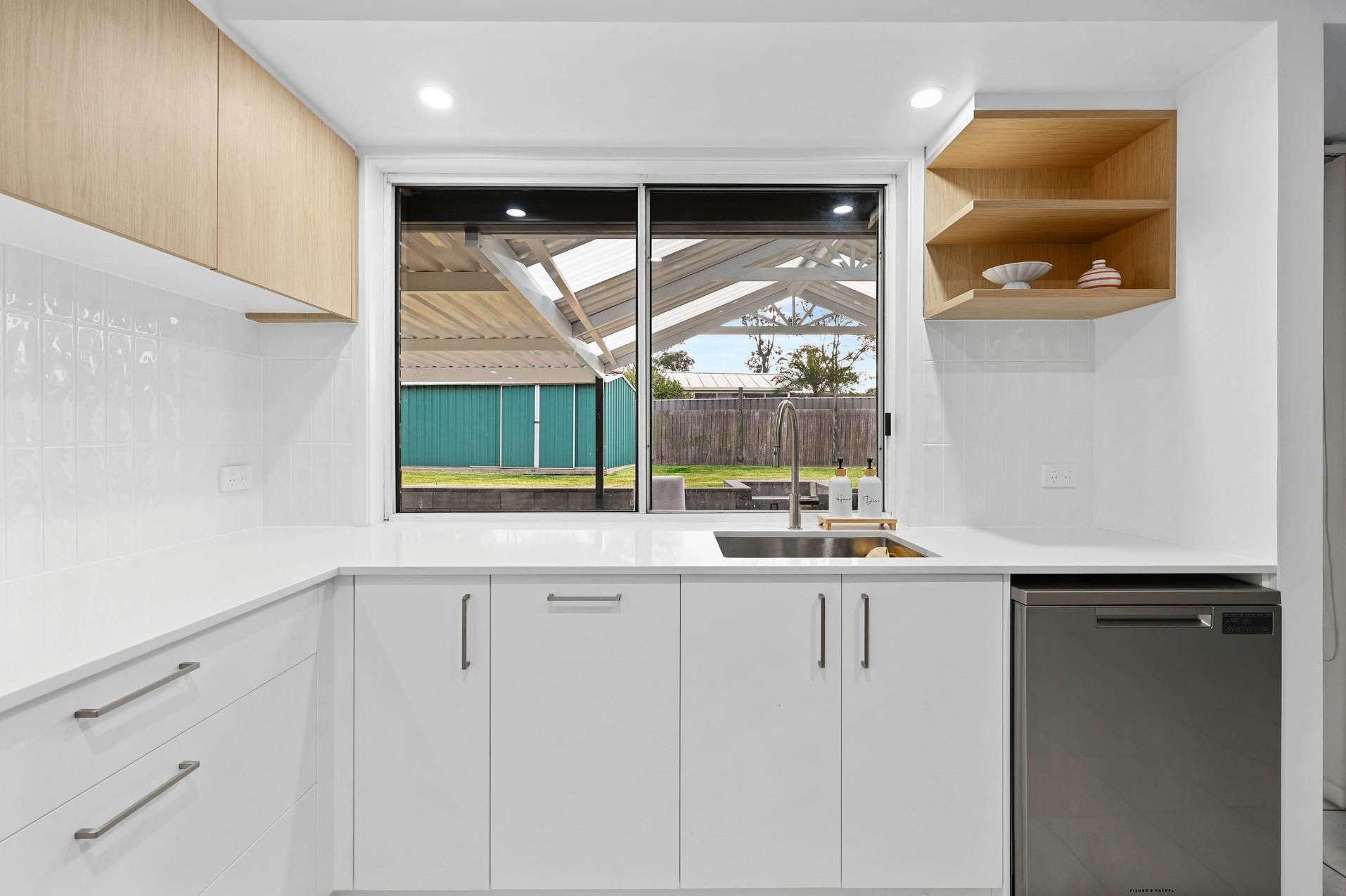 Modern White Kitchen with A Window Overlooking a Backyard. Wooden Shelves and Cabinets, Stainless Steel Appliances — Above & Beyond Interiors Custom Joinery in Currans Hill, NSW