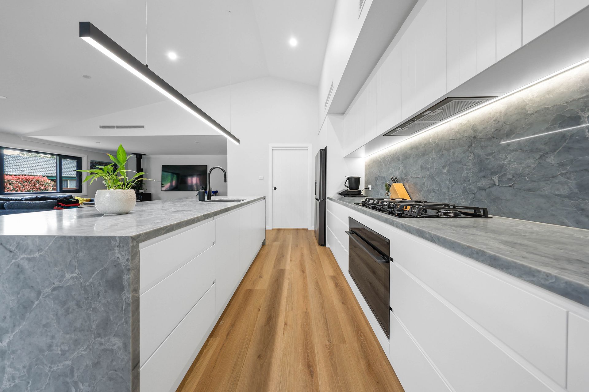Modern white kitchen with grey countertops and wood floor — Above & Beyond Interiors Custom Joinery in Bellambi, NSW