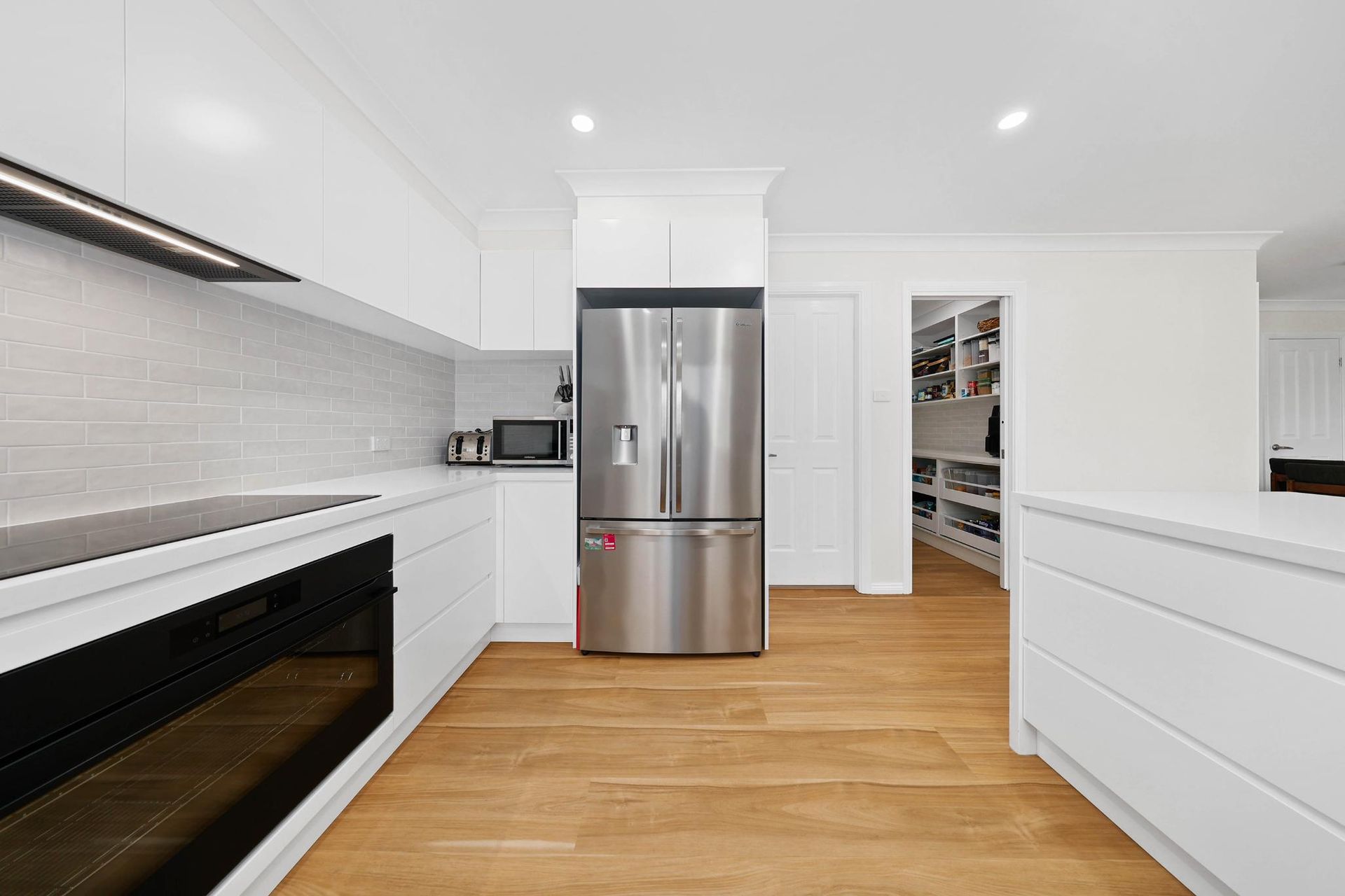 Modern Kitchen with White Cabinets, Stainless Steel Refrigerator, and Pantry — Above & Beyond Interiors Custom Joinery in Mount Anna, NSW