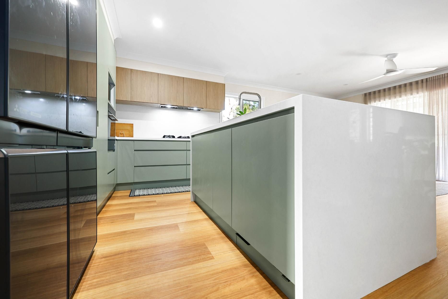 Modern Kitchen with White Island, Sage Green Cabinets, and Light Wood Flooring — Above & Beyond Interiors Custom Joinery in Holsworthy, NSW