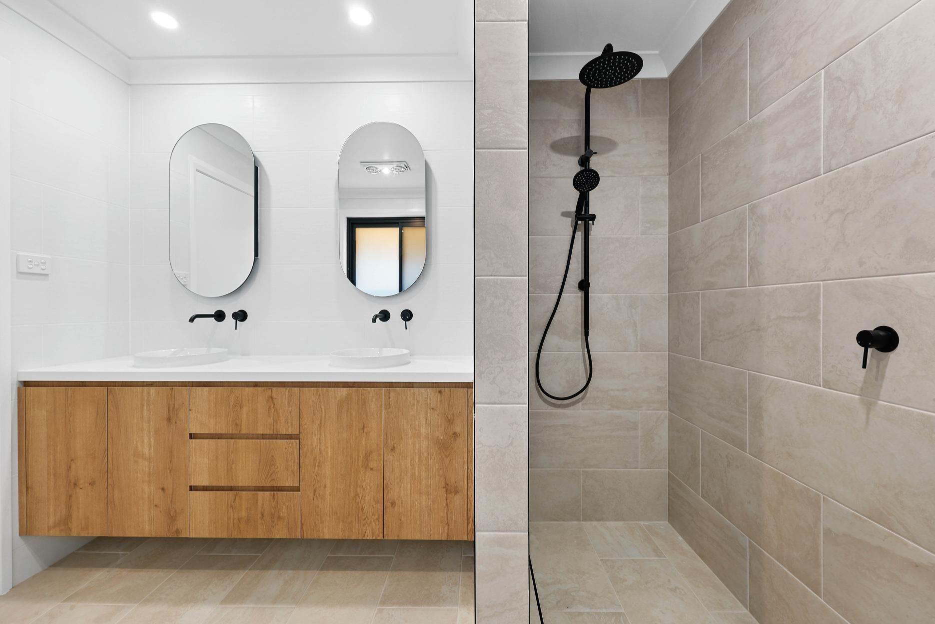 Bathroom with Wood Vanity, Oval Mirrors, and A Walk-In Shower with Black Fixtures — Above & Beyond Interiors Custom Joinery in Abbortsbury, NSW