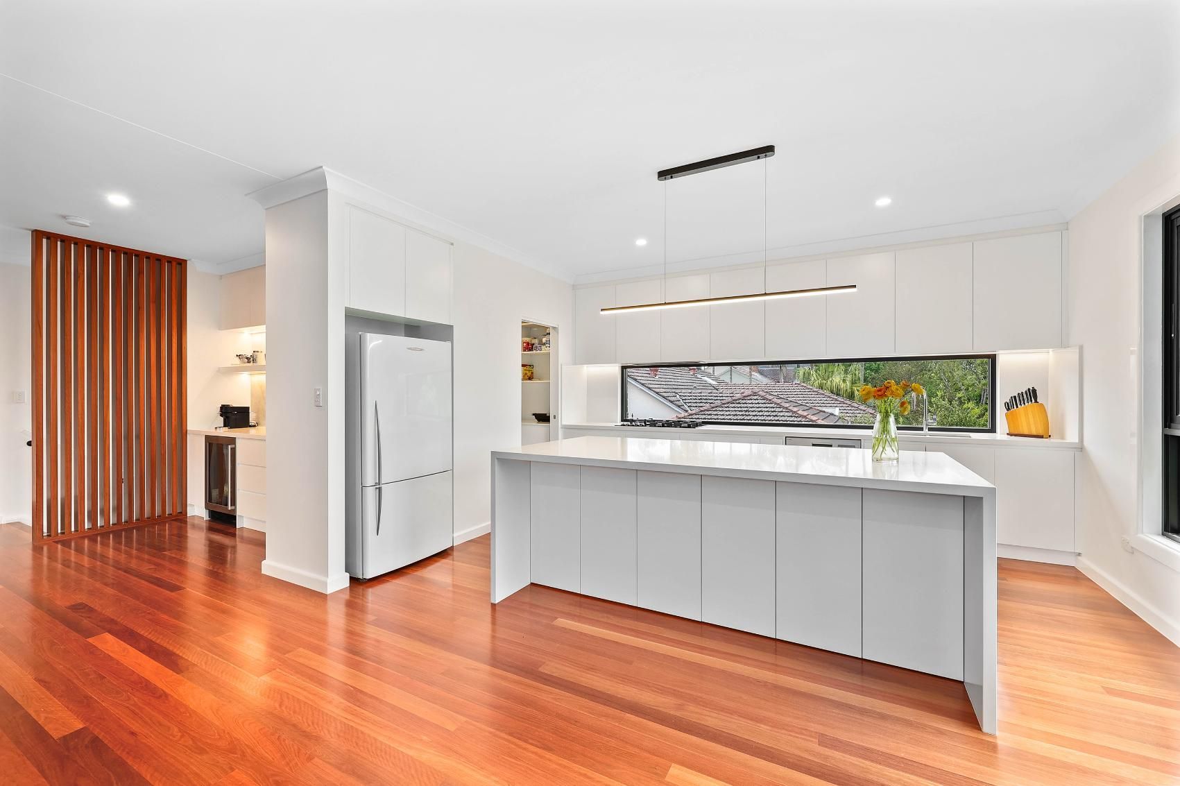 Modern White Kitchen with Island, Wood Floors, and Open Window — Above & Beyond Interiors Custom Joinery in Killara, NSW